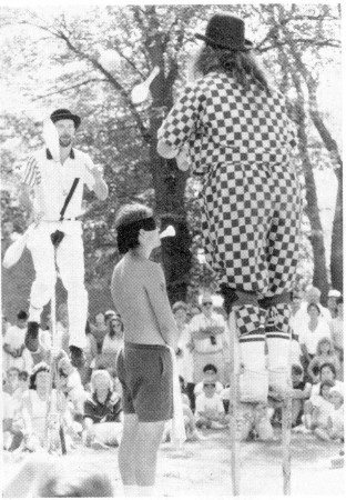 Johnny Toronto on unicycle & Madame Buskerfly on stilts pass clubs around a volunteer.